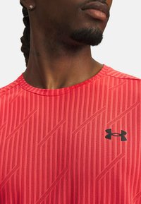 Punane spordipait, millel on tekstuuriga disain ja diagonaalsed triibud, ümmargune kaelus ning must Under Armour logo rinnal.