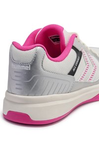 Zapatilla deportiva blanca con acentos en plata y rosa, que presenta un material texturizado, un collar acolchado y un logotipo negro. La suela es rosa y blanca.