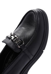 Mocassino in pelle nera con punta arrotondata, accentuato da una catena metallica e dettagli cuciti sulla tomaia, dotato di suola in gomma testurizzata.