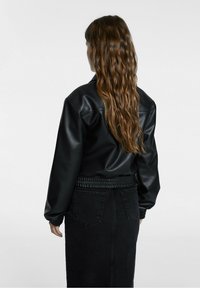 Veste bomber en faux cuir noir avec une coupe décontractée, taille côtelée et manches longues. Détail texturé visible aux poignets.