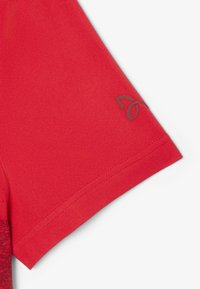 Röd kortärmad skjorta i strukturerad tyg, med en liten logotyp i en mörkare nyans vid ärmslutet. Släta sömmar och skräddarsydd passform.