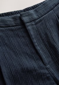 Mørkeblåt tekstureret stof med et ribbet mønster, med en elastisk talje med indsamlet kant og en flad frontdetalje.