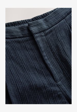 Tumed sinist värvi tekstureeritud kangas, millel on sooniline muster, voltidega kummiga vöökoht ja sile esiosa detail.