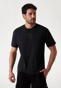Sort kortærmet t-shirt lavet af glat stof, med et let præget logo på brystet og en rund halsudskæring.