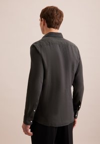 Camicia a maniche lunghe in tessuto grigio scuro, con colletto classico, polsini con bottone e una superficie leggermente strutturata.