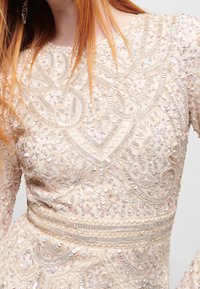 Beaded Kleid mit aufwendiger Stickerei in Cremefarbe, das Pailletten und strukturierte Muster aufweist. Lange Ärmel, figurbetonter Oberteil und eine Taillenband.