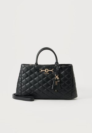 Sac à main matelassé noir Guess avec double poignée, accessoires dorés et porte-clés de marque attaché sur un fond clair uni.