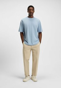 Light blue short-sleeve shirt with a round neckline, paired with beige pants and white sneakers. Smooth fabric, relaxed fit.