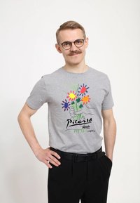 Šedé bavlněné tričko s barevným květinovým potiskem v ručně kresleném stylu, černým písmem a krátkými rukávy, doplněné černými kalhotami.