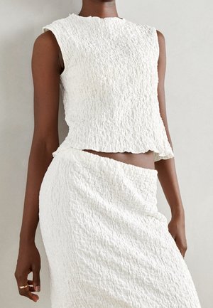 Weißes ärmelloses Oberteil mit strukturiertem Stoff und gewelltem Saum, kombiniert mit einem passenden strukturierten Rock, beide mit figurschmeichelndem Schnitt.
