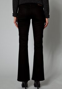 Mustat levenevät farkut, joissa on sileä pinta, takataskut ja korkea vyötärö, hillityllä kuviolla. Yhdistetty korkeakorkoisiin kenkiin.