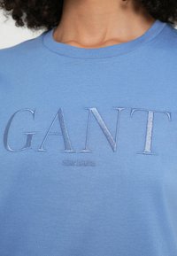 Kék pamut póló hímzett "GANT" logóval sötétebb kék színben. Kerek nyakkivágással és rövid ujjal, sima textúrával.