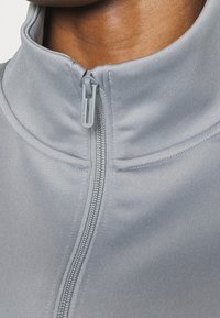 Gros plan sur le cou d'une personne portant une veste gris clair à fermeture éclair totalement fermée jusqu'au col montant.