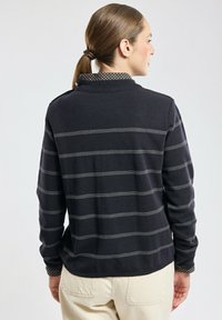 Polo con maniche lunghe di colore nero, con righe orizzontali grigie e un colletto decorato. Realizzato in tessuto morbido, con vestibilità rilassata e polsini a coste.