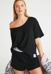 Must mustriba off-shoulder topp, millel on mustad lühikesed püksid, millel on kontrastne vöökoht, sujuva tekstuuri ja mugava lõikega.