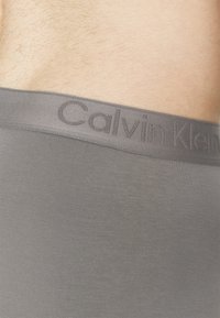 Boxer briefs grigi con una texture liscia presentano un cinturino con logo, mostrando il design minimalista tipico dei prodotti Calvin Klein.
