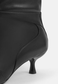 Black leather ankle boot with smooth texture, fitted design, curved side seams, and a short stiletto heel.