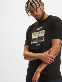 Sort bomulds t-shirt med grafisk tryk af en hjørnebutik med tekstlabels. Korte ærmer og rund halsudskæring. Løs pasform.