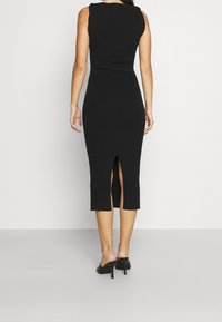 Schwarzes, geripptes Midi-Kleid mit tailliertem Schnitt, das einen Rückenschlitz und ärmelloses Design aufweist. Das Material wirkt weich und strukturiert.