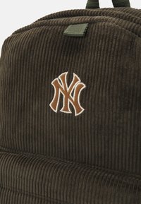 Sac à dos en velours côtelé marron avec des rayures verticales, une surface texturée et un logo NY brodé dans des accents marron et blanc.