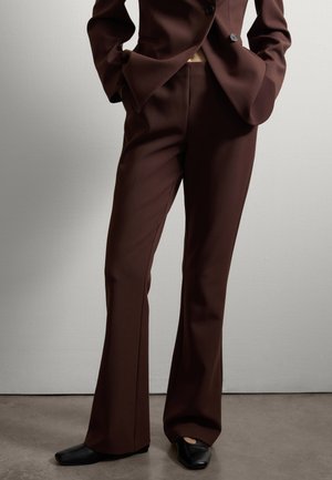 Brown tailored suit trousers, featuring a flared design, smooth texture, and a clean, seam detail along the legs. Paired with black shoes.