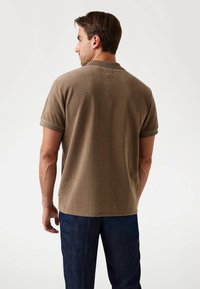 Polo shirt marron à motif en chevrons avec une texture douce, arborant un col et des poignets contrastés. Porté avec un pantalon bleu foncé.
