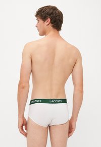 Weiße Slips mit einem grünen Lacoste-Logo-Bund, aus weichem Material, mit enganliegender Passform und minimalistischem Design.
