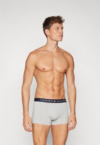 Graue Baumwollboxershorts mit einem marineblauen Bund, der das "TOMMY HILFIGER"-Logo in Weiß zeigt, glatte Textur, eng anliegendes Design.