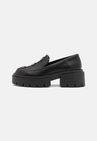 Mustat loafers, joissa on paksut, uritetut pohjat, sileä nahkainen yläosa ja koristeellinen hopeinen varuste vampin alueella. Määritelty muoto, jossa on pyöristetty kärki.