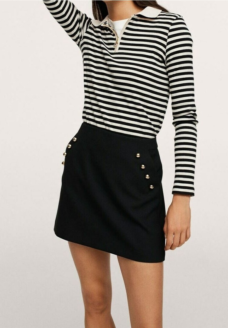 Polo a maniche lunghe a righe bianche e nere con zip e colletto bianco, abbinato a una mini gonna nera con dettagli in bottone dorato.