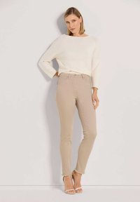 Beige high-waisted skinny jeans with a frayed hem, paired with a cropped white textured sweater and strappy beige heels.