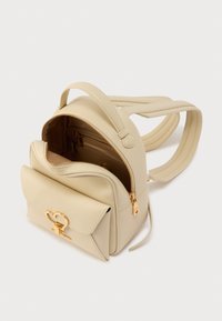 Μπεζ δερμάτινο σακίδιο με τσέπη στο μπροστινό μέρος με καπάκι, χρυσά μεταλλικά στοιχεία, διπλές θήκες με φερμουάρ και ρυθμιζόμενους ιμάντες. Ομαλή υφή, δομημένος σχεδιασμός.