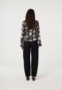 Zwarte blouse met een patroon van abstracte witte ontwerpen, gecombineerd met zwarte wijde broek. De stof lijkt glad met ontspannen mouwen.
