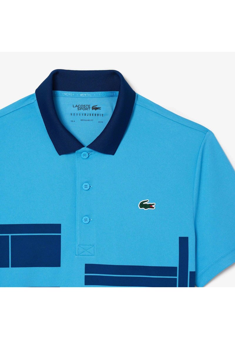 Polo bleu clair avec col marine. Présente un tissu texturé et deux boutons. Comprend des motifs géométriques bleu foncé et le logo Lacoste.