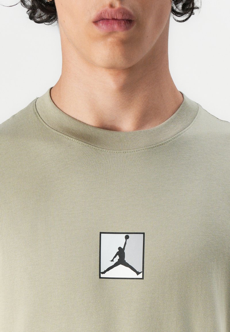 T-shirt en coton vert olive avec un patch logo Jumpman en noir et blanc sur la poitrine. Encolure ronde avec texture côtelée.