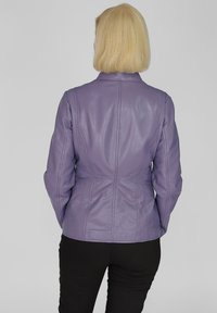 Lila läderjacka med en åtsittande design, med vertikala sömmar och ståkrage. Buren över svarta byxor.
