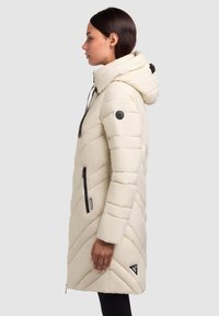 Piumino beige chiaro con cappuccio, dotato di cuciture a zigzag, zip nere e un'etichetta con logo sulla manica.