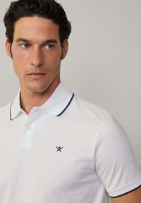 Polo bianco con bordino blu navy sul colletto, con un piccolo logo nero sul petto, realizzato in un morbido misto cotone.