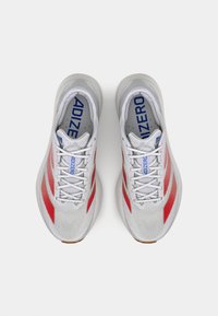 Lichte hardloopschoenen met een grijze mesh bovenkant, rode diagonale strepen, witte veters en een gevoerde tong waarop "ADIZERO" in het blauw staat.