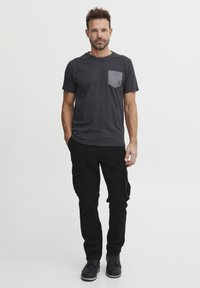 Grå t-skjorte med korte ermer og kontrastlomme, sammen med svarte cargo-bukser med sidelommer og svarte støvler. Enkel, uformell design.