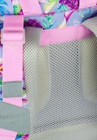 Vnitřek síťovaného batohu obsahující světle šedou síťovanou kapsu, růžové popruhy a látku s květinovým vzorem. Odolný materiál s prodyšnou texturou.