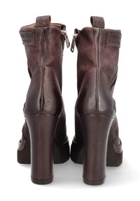Botas de tobillo de cuero marrón con un alto tacón cuadrado, que cuentan con cremalleras en los laterales y superficies texturizadas. Incluyen una lengüeta en la parte posterior.