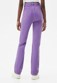 Fioletowe dżinsy z wysokim stanem, proste nogawki i tylne kieszenie, wykonane z materiału dżinsowego. Noszone z białymi sneakersami na platformie.
