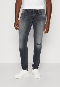 Tmavě šedé džíny z denimu s úzkým střihem, jemně ošoupané a vybledlé, doplněné bílými teniskami a přiléhavým bílým tričkem.