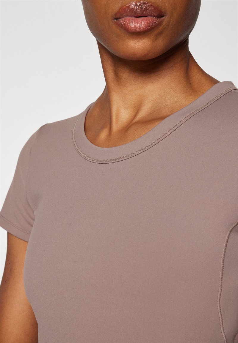 Haut ajusté à manches courtes dans une couleur mauve douce. Texture lisse avec un col rond et un détail de couture subtil le long des bords.