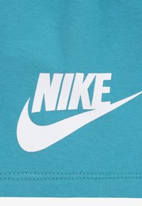 Tyrkysová látka s velkým bílým logem "Nike" a designem swoosh, s hladkým povrchem a prošívanými okraji.