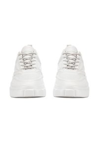 Zapatos deportivos blancos con parte superior texturizada, lengüeta acolchada y suela gruesa y robusta. Presentan cordones grises y detalles minimalistas de diseño.