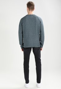 Suéter texturizado en azul grisáceo claro con cuello redondo, mangas largas y ajuste holgado, combinado con pantalones negros y zapatos blancos.