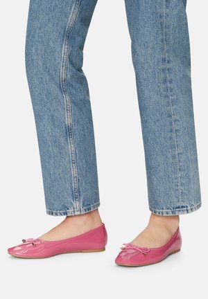 Glänzende rosa Ballerinas mit spitz zulaufender Zehenpartie, versehen mit einer kleinen Schleife und goldfarbenen Applikationen, kombiniert mit hellblauen Jeans mit geradem Bein.