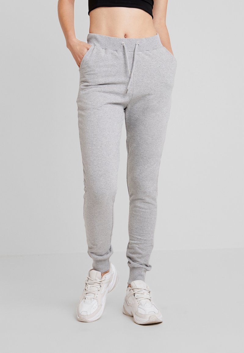 Grå bomullsjoggers med sidofickor, elastisk midja och snörning, åtsittande vid anklarna. Bärs med vita sneakers.